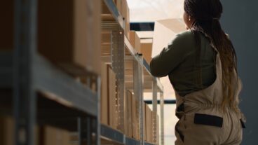 Chief logistics officer in warehouse arranging cardboard boxes full of merchandise ready to be shipped to clients