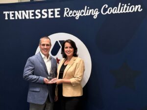 Kingsport mill manager Troy Wilson and public affairs director Jan Martin accept Kingsport's recycling awared from the Tennessee Recycling Coalition. Man and woman holding award in front of banner that says Tennessee Recycling Coalition.