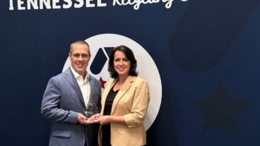 Kingsport mill manager Troy Wilson and public affairs director Jan Martin accept Kingsport's recycling awared from the Tennessee Recycling Coalition. Man and woman holding award in front of banner that says Tennessee Recycling Coalition.