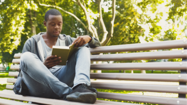Black man reading on park bench. May is Get Caught Reading Month.