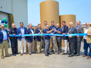 Celebrating the Kingsport grand reopening - Group of Domtar and local, state, federal dignitaries cutting a blue ribbon in front of finished rolls of containerboard. They are outside.